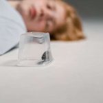 woman lying down out of focus near a trapped roach in a plastic case